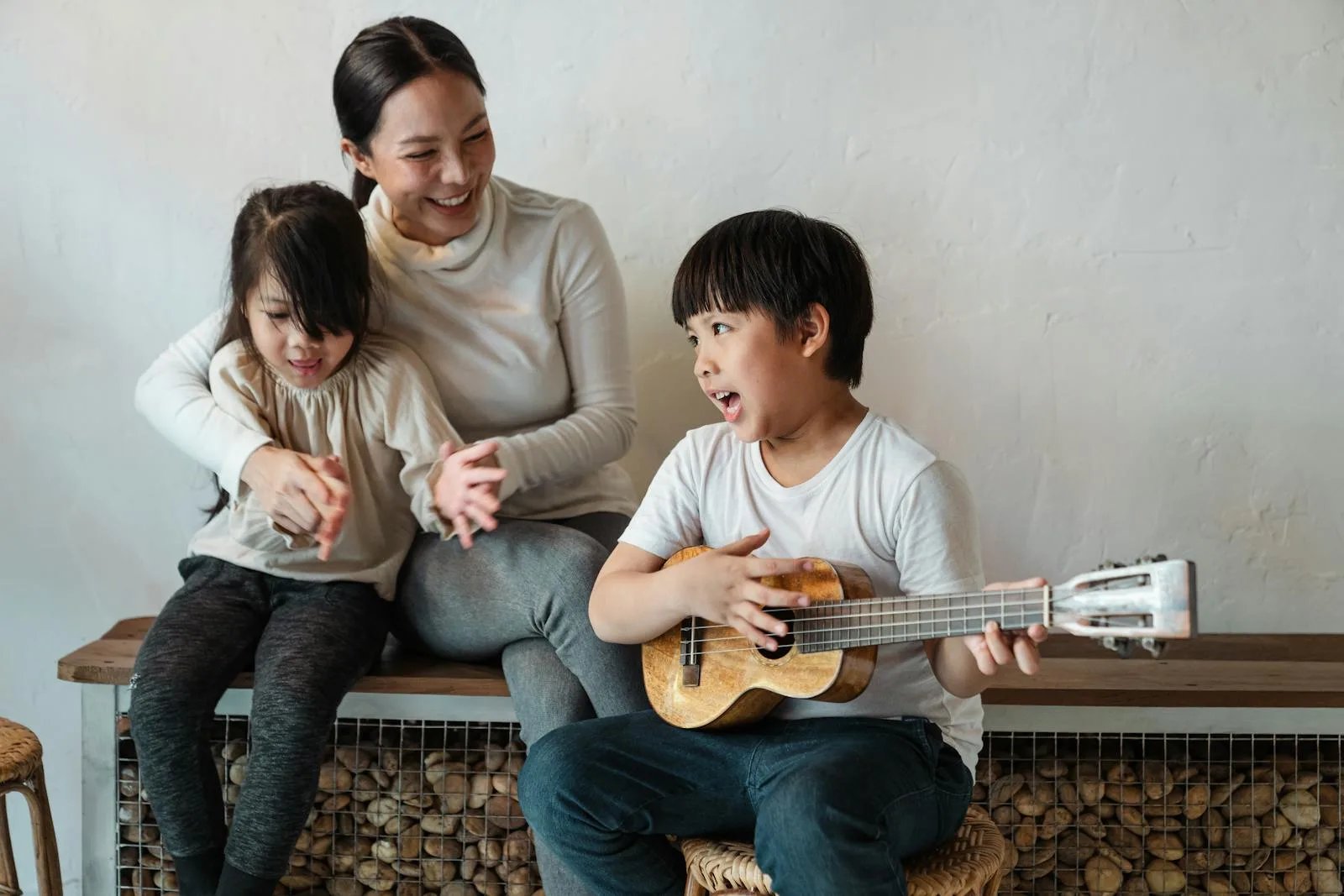 A joyful family moment with a mother and two children playing a ukulele indoors.