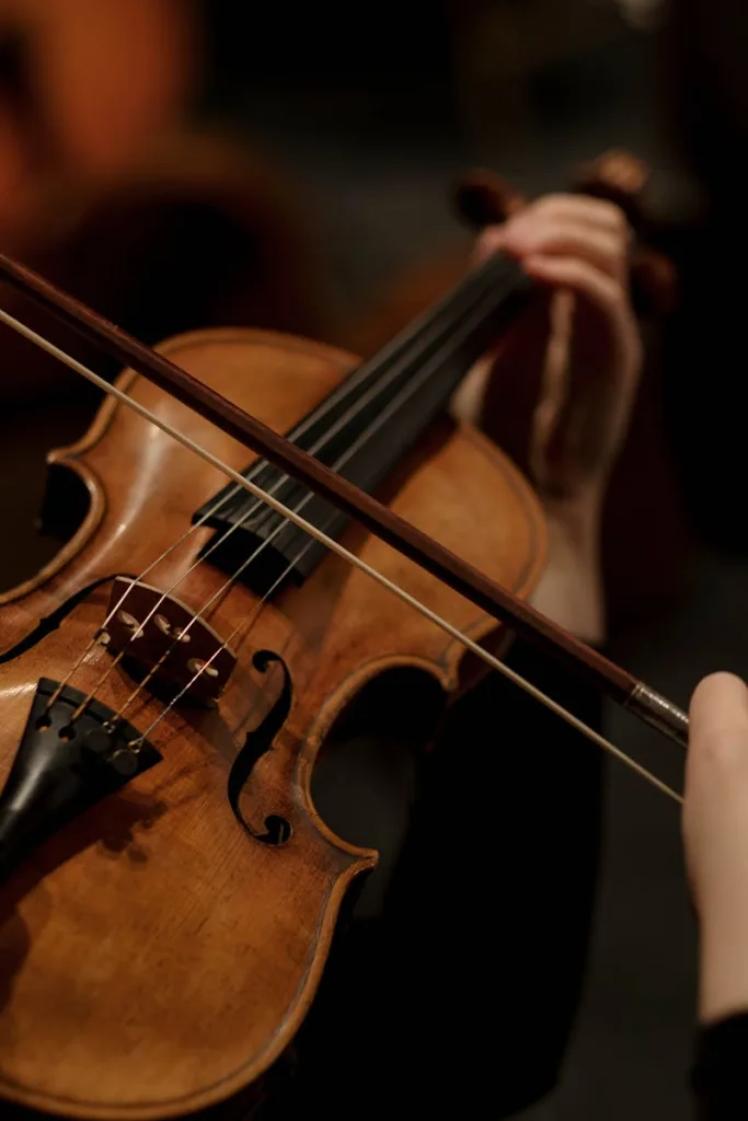 Detailed shot of hands playing a violin, highlighting the strings and bow in a dim setting.