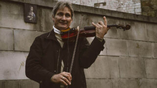 smiling standing man playing violin by gray stone wall