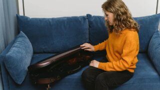 a woman opening a violin case while sitting on a couch